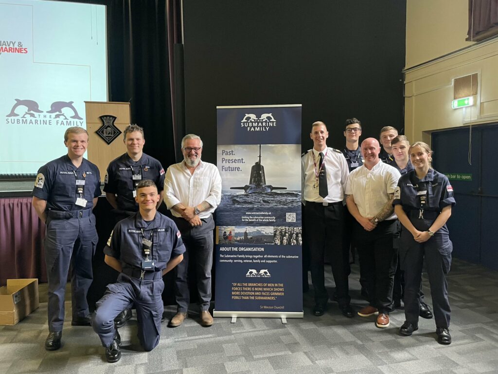Instructors, trainees and the CO of HMS Sultan around a The Submarine Family banner.